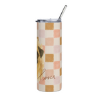 A tall insulated tumbler with a clear lid and metal straw, featuring a watercolor-style dog illustration and a pastel checkerboard pattern in pink, peach, tan, and cream, with the word 'lover' in script near the bottom.